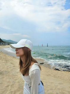 a young woman standing on top of a sandy beach next to the ocean with boats in the water