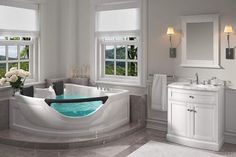 a large white bath tub sitting next to two sinks in a bathroom under three windows