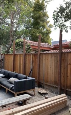 a couch sitting in the middle of a yard next to a fence and wooden posts