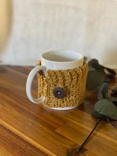 a crocheted coffee cup with a button on the side sitting on a wooden table