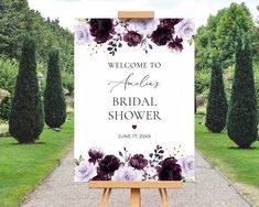 a welcome sign with flowers on it in front of some trees and bushes, for an outdoor bridal shower