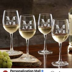 four wine glasses with the letter m on them next to some grapes and a bottle of wine