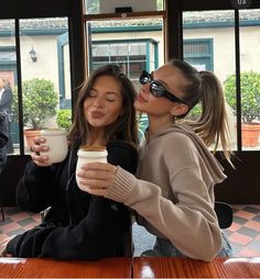 two women sitting at a table drinking coffee and kissing each other with their eyes closed