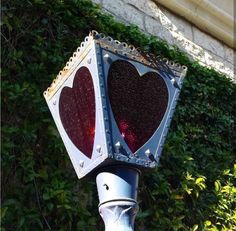 a street light with two hearts painted on it's side and some bushes behind it