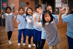 a group of young children standing on top of a wooden floor holding their hands in the air