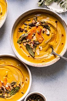 three bowls filled with pumpkin soup and topped with toasted pumpkins, nuts, and sage