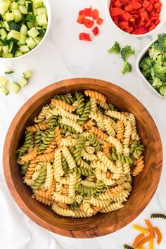 a bowl filled with pasta and vegetables next to bowls of broccoli, carrots, celery