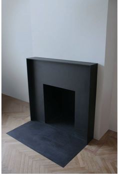 an empty black fireplace in a room with parquet floor and white wall behind it