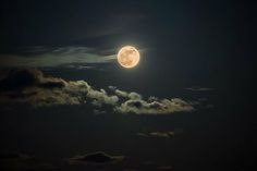 the full moon is shining brightly in the night sky with clouds and dark blue skies