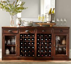 a buffet table with wine bottles and glasses on it, next to a vase filled with flowers