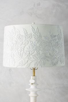 a table lamp with a white fabric shade on it and a gold metal base in the middle