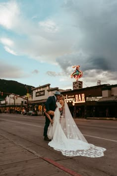 a bride and groom kissing on the street in front of an old fashioned neon sign