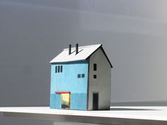 a small blue house sitting on top of a white table next to a gray wall