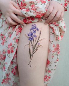 a woman's thigh with a flower tattoo on the side and purple flowers around it