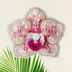 a flower made out of beads and pearls on a white background with a palm tree in the foreground