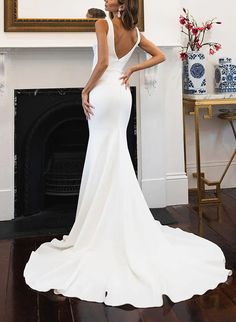 a woman standing in front of a fireplace with her back turned to the camera wearing a white dress