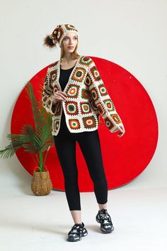 a woman standing in front of a red circle wearing a crocheted jacket and black leggings