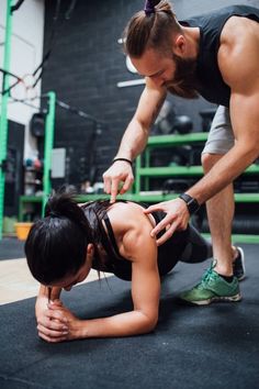 a man helping a woman with her leg on the ground in a gym area,