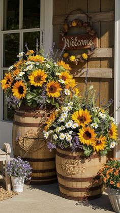 two large wooden barrels filled with flowers sitting on the side of a building next to a welcome sign