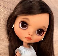 a close up of a doll with long black hair and big brown eyes, wearing a white dress