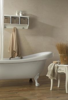 a white bath tub sitting on top of a hard wood floor next to a shelf