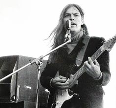 a man with long hair playing guitar in front of a microphone and another person standing behind him