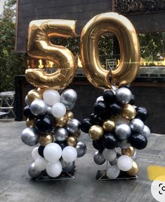 two black and white balloons with the number 50 in front of a building that is decorated with gold and silver balloons