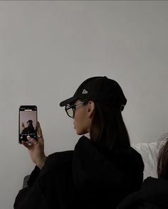 a woman taking a selfie with her cell phone while wearing a hat and glasses