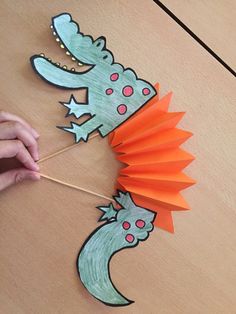 someone is making a paper dinosaur puppet on the floor with an orange and green pinwheel