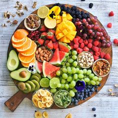 a wooden platter filled with fruits, nuts and fruit salads on top of a white table