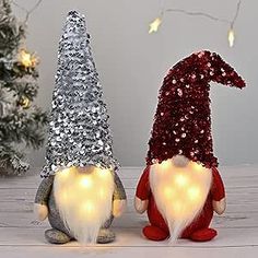 two gnomes sitting next to each other in front of a christmas tree with lights