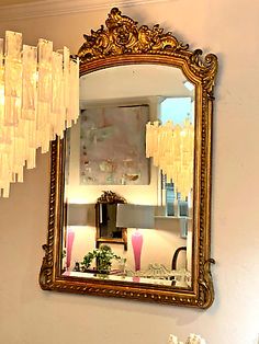 a mirror hanging on the wall next to a table with flowers and vases in it