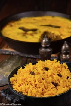 two pans filled with yellow rice on top of a wooden table