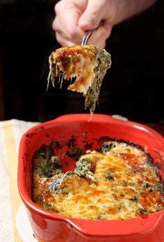 a person is taking a piece of pizza from a red casserole dish