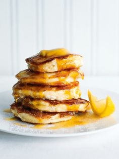 a stack of pancakes with syrup and lemon wedges on a white plate against a white wall