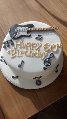 a white birthday cake with musical notes and guitar on the top is sitting on a wooden table