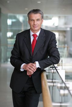 a man in a suit and red tie leaning on a railing with his arms crossed