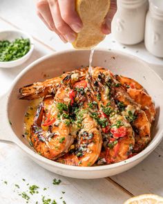 a person dipping sauce on top of shrimp in a white bowl with lemon wedges