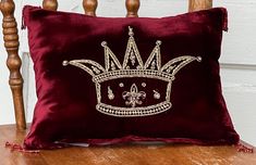 a red pillow with a gold crown on it sitting on a wooden chair next to a white wall