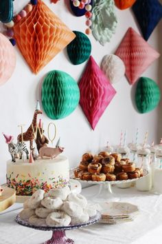 a table topped with cakes and desserts next to paper decorations hanging on the wall