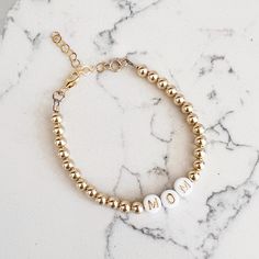 Made of high quality 14k gold filled beads, the NEW Luxe Gold Filled Mom Bracelet makes the sweetest gift or treat for yourself. Great on its own or paired with a watch — always amazing layered. One beaded bracelet Size: 6” + 1.5” gold filled extender 5mm high quality 14k gold filled beads Lobster clasp Does not turn, tarnish, or rust Handmade with the highest standards & quality materials Includes 100% organic cotton jewelry pouch This item is made to order and shipped with love from our studio Adjustable Everyday Gold Bracelet For Mother's Day, Adjustable 14k Gold-filled Gold Charm Bracelet, 14k Gold Bracelet With Gold Beads As Gift, Everyday 14k Gold-filled Bracelets With Gold Beads, Everyday Bracelets With 14k Gold Beads, Personalized Adjustable Gold Bracelet For Everyday, Yellow Gold Bracelets For Everyday And Mother's Day, Everyday Adjustable Personalized Gold Bracelet, Gold Name Bracelet With Letter Beads