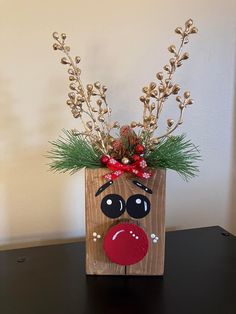 a wooden block with some plants in it and a reindeer face painted on the side