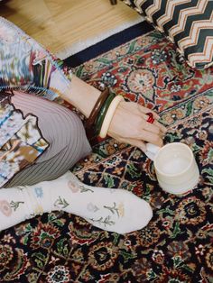 a woman is sitting on the floor with her feet up and holding a cup in one hand