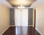 an empty living room with hard wood flooring and white drapes on the windows