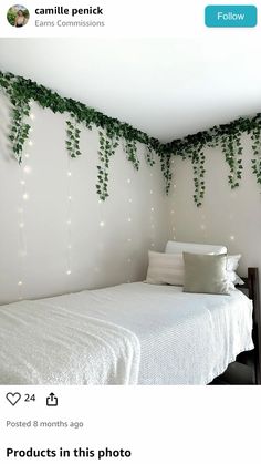 a white bed sitting next to a wall covered in green ivy vines and lights on it