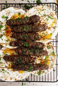 several skewered meats on top of tortillas with sauce and parsley