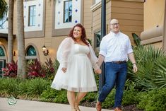 a man and woman holding hands while walking down the sidewalk in front of a hotel