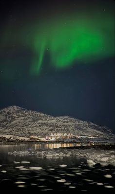 the northern lights shine brightly in the night sky over water and snow covered mountains,