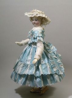 an old fashion doll wearing a blue dress and hat with ruffles on it