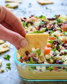 a hand dipping a tortilla chip into a salad